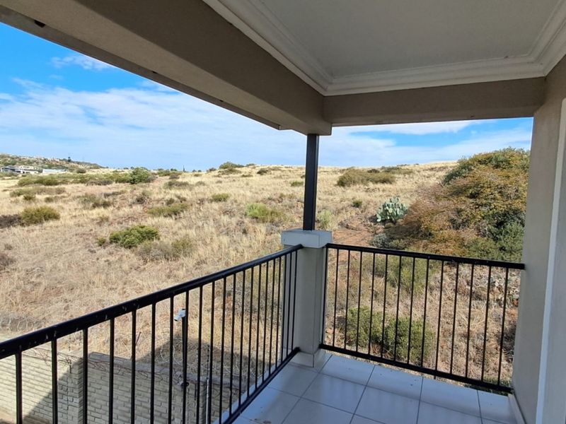A covered balcony featuring tiled flooring and a metal balustrade, offering an open view of the surrounding natural landscape.