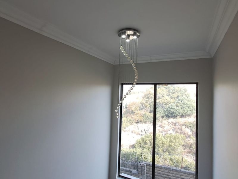 A bright, empty room featuring a modern spiral pendant light fixture, decorative ceiling cornices, and a window with a view of the surrounding landscape.