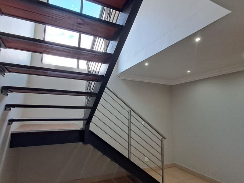 A bright, modern hallway featuring an open-tread staircase with metal balustrades, tiled flooring, and recessed downlighting.