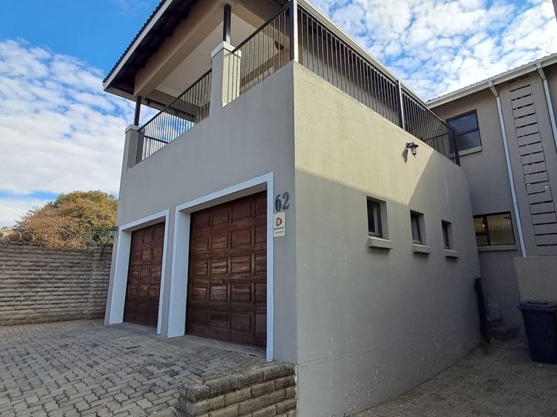 Exterior view of a townhouse featuring a double garage with wooden doors and an upper-level balcony with metal railings.