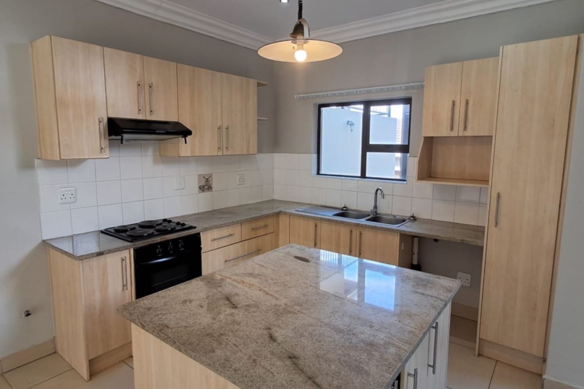 Modern kitchen featuring light wood cabinetry, granite countertops, a central island, built-in oven, gas hob, and tiled flooring in a clean, open layout.