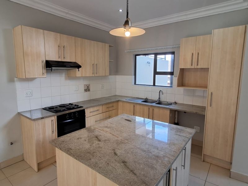 Modern kitchen featuring light wood cabinetry, granite countertops, a central island, built-in oven, gas hob, and tiled flooring in a clean, open layout.