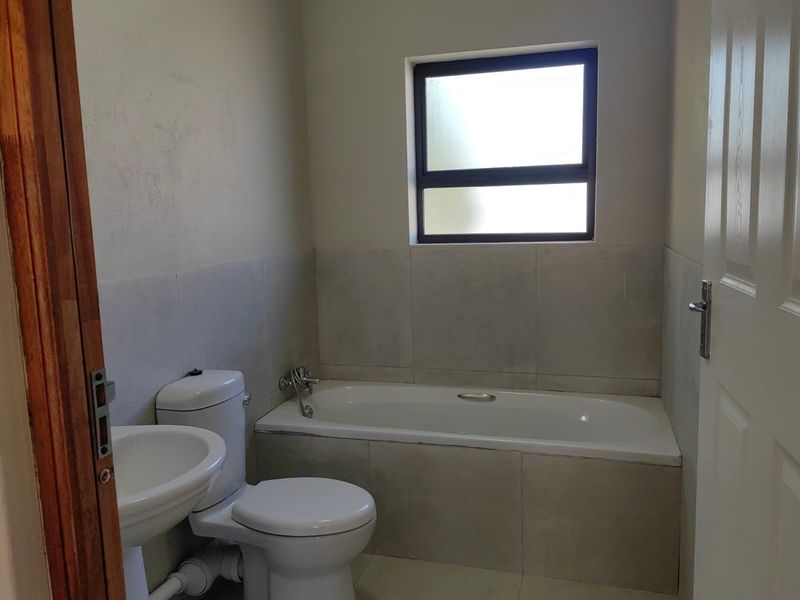 A functional bathroom featuring a bathtub, pedestal sink, and toilet with neutral wall tiling and a window for natural light.