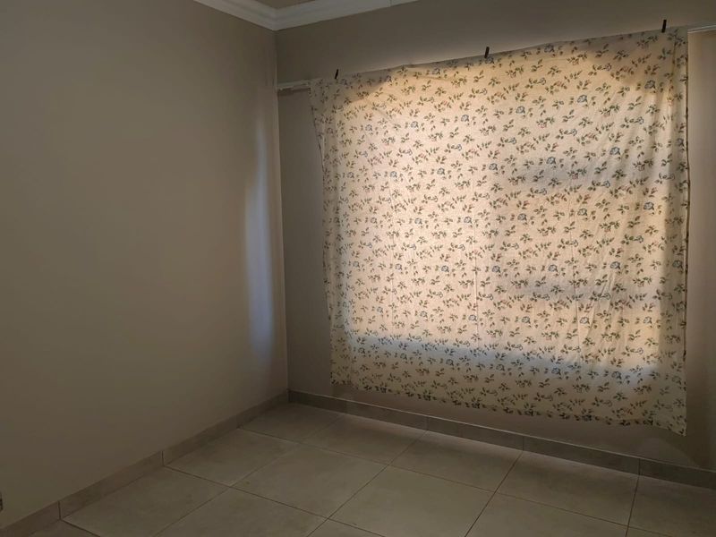 An empty bedroom featuring neutral wall paint, tiled flooring, and a large window covered by a floral curtain.