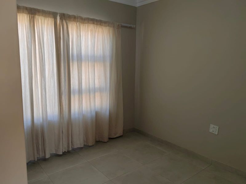A vacant bedroom featuring neutral wall paint, tiled flooring, and a curtain rod installed above the window.