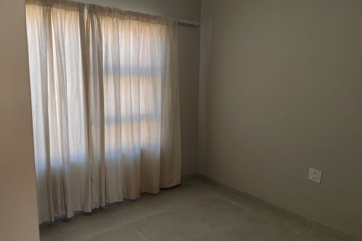 A vacant bedroom featuring neutral wall paint, tiled flooring, and a curtain rod installed above the window.