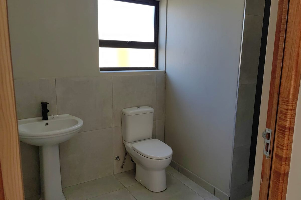 A clean, modern bathroom featuring a pedestal basin, toilet, and neutral wall and floor tiling with a window for natural light.