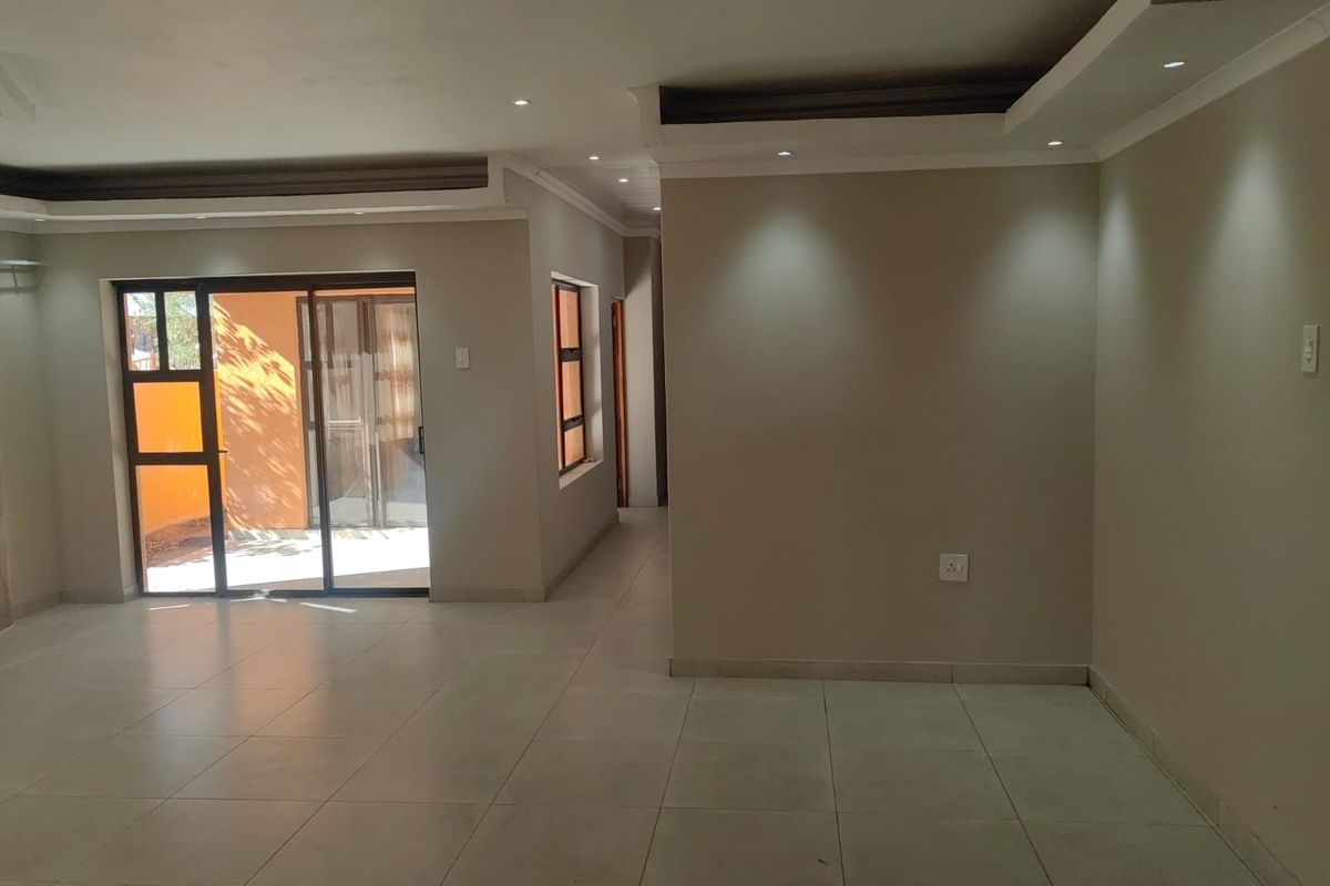 A spacious, empty living area featuring neutral tiled floors, recessed ceiling lighting, and a sliding glass door providing access to the exterior.