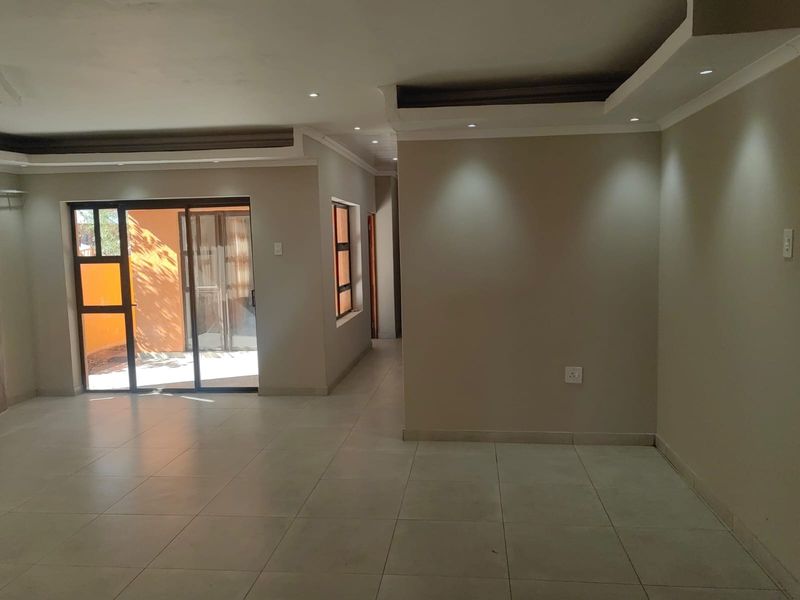 A spacious, empty living area featuring neutral tiled floors, recessed ceiling lighting, and a sliding glass door providing access to the exterior.
