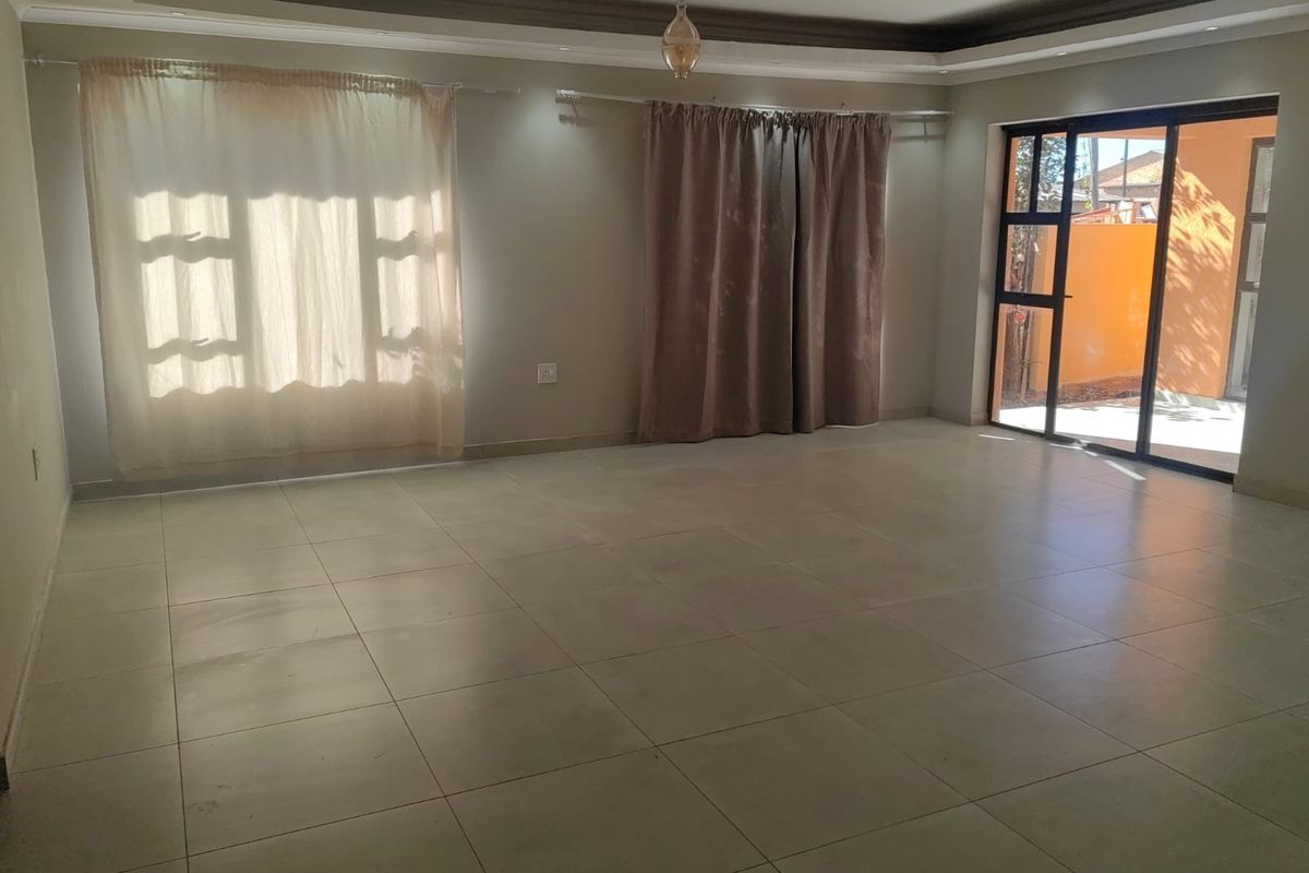 Spacious, empty living area featuring neutral tiled flooring, recessed ceiling details, and a large sliding glass door providing access to the exterior.