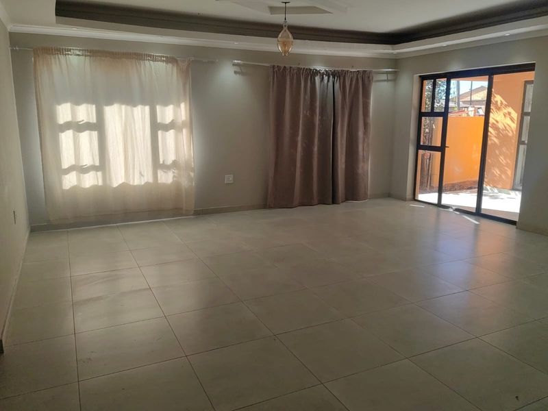 Spacious, empty living area featuring neutral tiled flooring, recessed ceiling details, and a large sliding glass door providing access to the exterior.