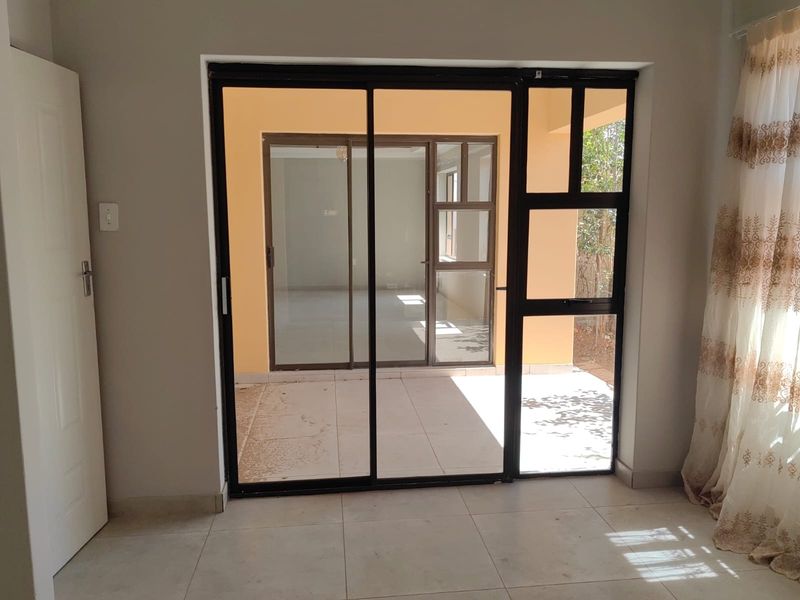 A bright living area featuring tiled flooring and a large sliding glass door providing access to an outdoor patio space.