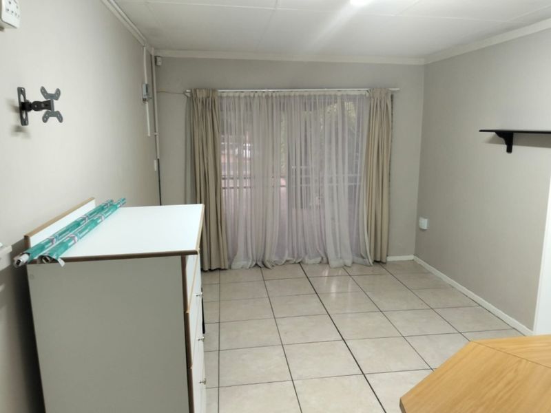 A simple, tiled living area featuring a sliding glass door with curtains and wall-mounted fixtures, offering a neutral space ready for personalization.