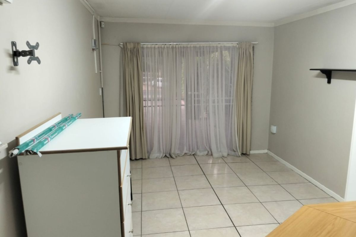 A simple, tiled living area featuring a sliding glass door with curtains and wall-mounted fixtures, offering a neutral space ready for personalization.