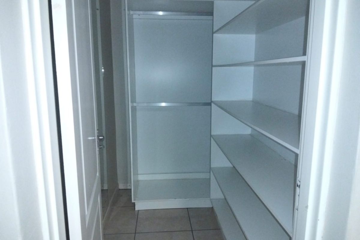 A walk-in closet or dressing area featuring built-in white cabinetry with shelving and hanging rails, finished with neutral floor tiles.