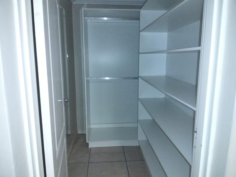 A walk-in closet or dressing area featuring built-in white cabinetry with shelving and hanging rails, finished with neutral floor tiles.
