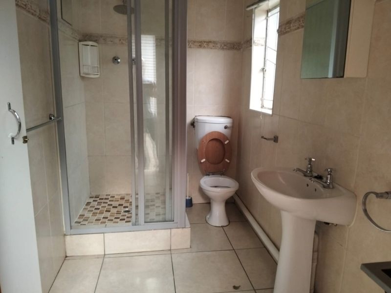 A functional bathroom featuring a shower enclosure, pedestal basin, and toilet with neutral wall and floor tiling.