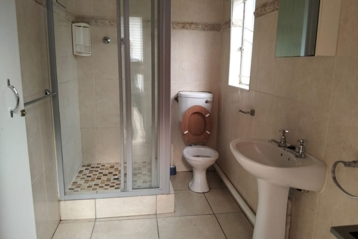 A functional bathroom featuring a shower enclosure, pedestal basin, and toilet with neutral wall and floor tiling.