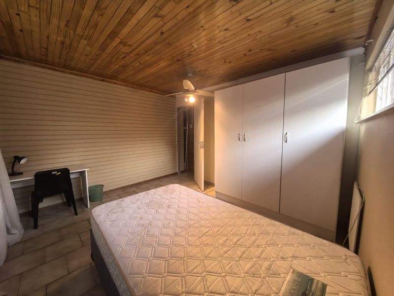 A bedroom featuring built-in cupboards, a timber-clad ceiling with a ceiling fan, and tiled flooring.