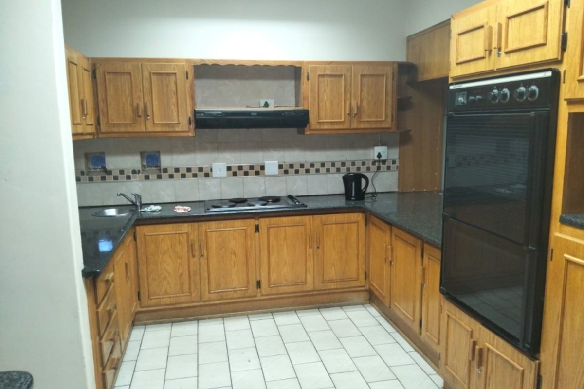 A functional kitchen featuring traditional wooden cabinetry, granite countertops, a built-in oven, and an electric hob with an extractor fan.