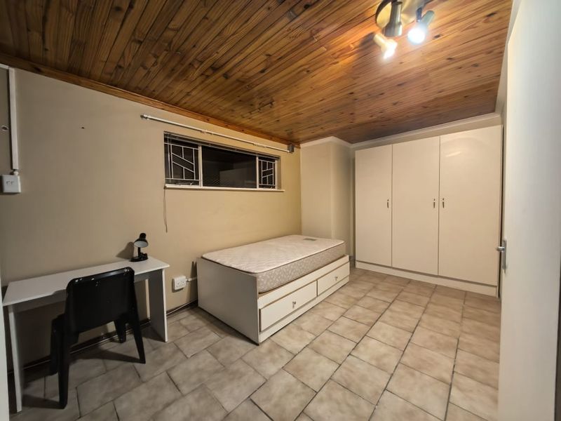 A bedroom featuring built-in cupboards, tiled flooring, and a timber-clad ceiling, providing a functional space with basic finishes.