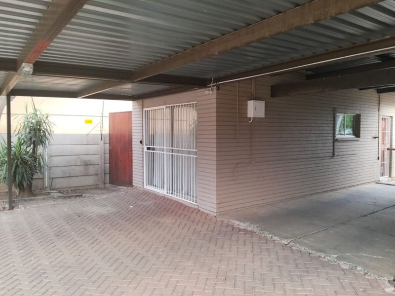A covered carport area featuring a corrugated metal roof, paved driveway, and secure sliding door access to the main building.
