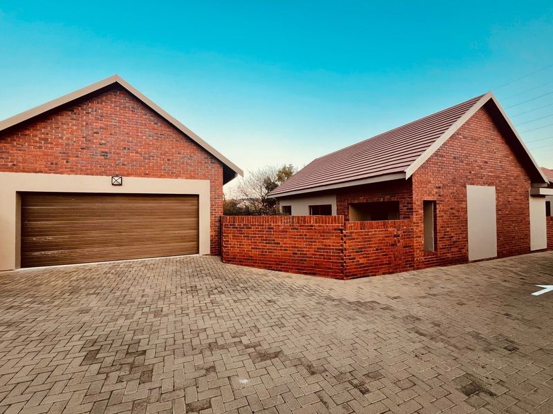 A modern townhouse exterior featuring a face-brick facade, tiled roof, and a spacious paved driveway leading to a secure garage.