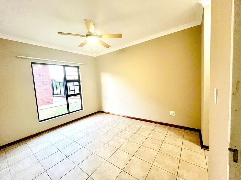 A bright, empty bedroom featuring neutral wall tones, tiled flooring, and a ceiling fan, offering a clean canvas for personalization.
