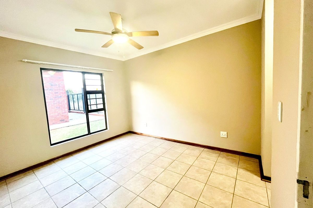 A bright, empty bedroom featuring neutral wall tones, tiled flooring, and a ceiling fan, offering a clean canvas for personalization.