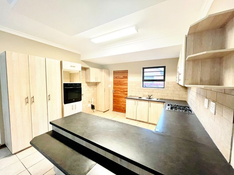 A clean and functional kitchen featuring light wood cabinetry, dark laminate countertops, a built-in oven, gas hob, and tiled backsplash.