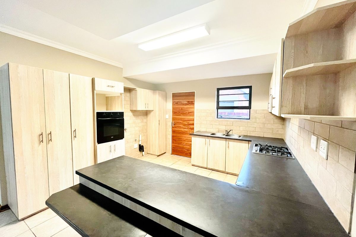 A clean and functional kitchen featuring light wood cabinetry, dark laminate countertops, a built-in oven, gas hob, and tiled backsplash.
