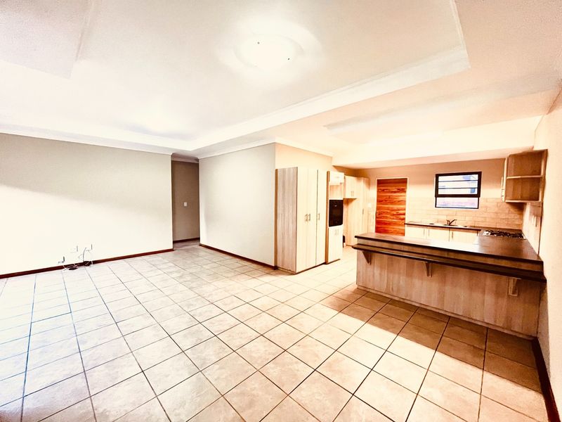 Spacious open-plan living and kitchen area featuring tiled flooring, built-in cabinetry, a breakfast bar, and integrated cooking appliances.