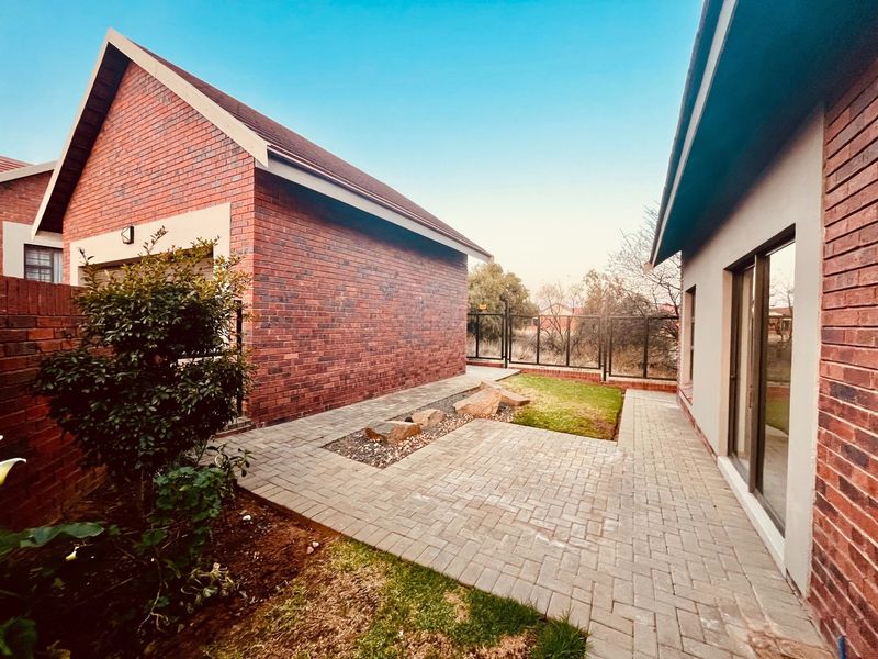 A well-maintained rear exterior view of the townhouse featuring a paved patio area, brick facade, and access via sliding glass doors.