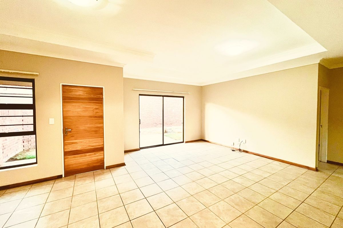 Spacious, empty living area featuring neutral tiled flooring, a modern wooden door, and a sliding glass door providing access to the exterior.