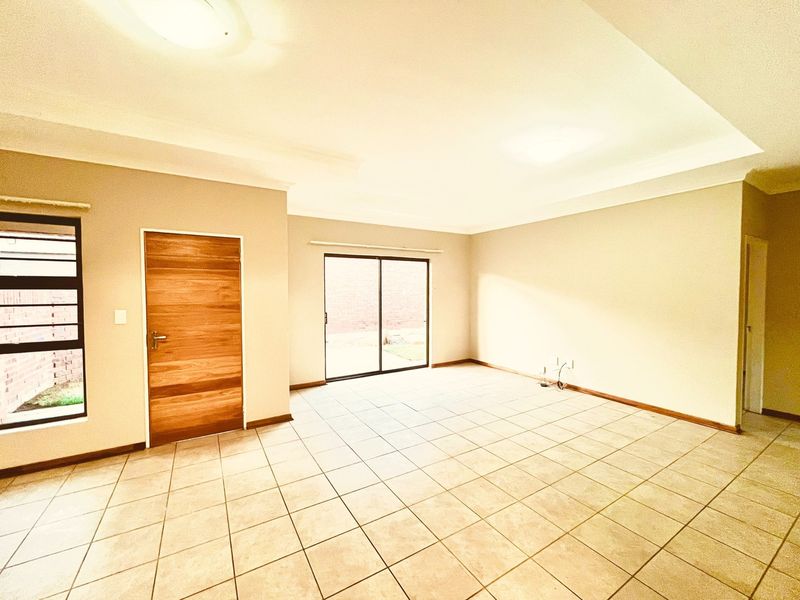 Spacious, empty living area featuring neutral tiled flooring, a modern wooden door, and a sliding glass door providing access to the exterior.