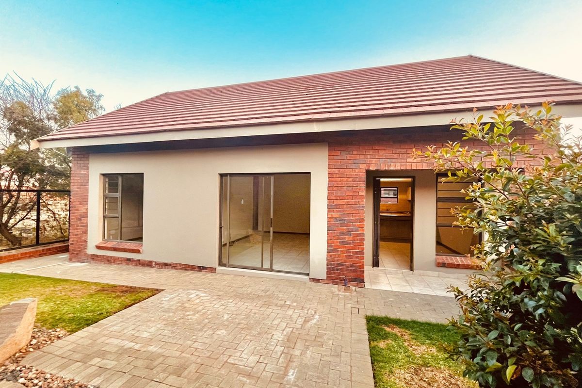 Rear view of a townhouse featuring a brick and plaster facade, tiled roof, paved patio area, and sliding glass doors leading to the interior.