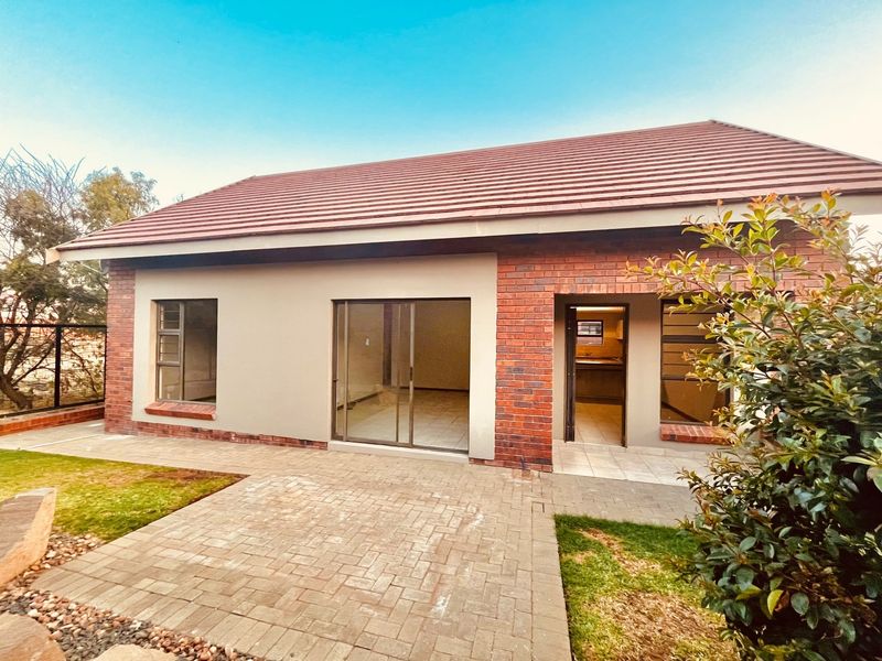 Rear view of a townhouse featuring a brick and plaster facade, tiled roof, paved patio area, and sliding glass doors leading to the interior.