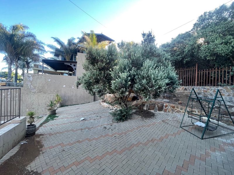 Rear garden area featuring paved patio space, stone retaining walls, and perimeter fencing, requiring maintenance to the boundary wall and paving surfaces.