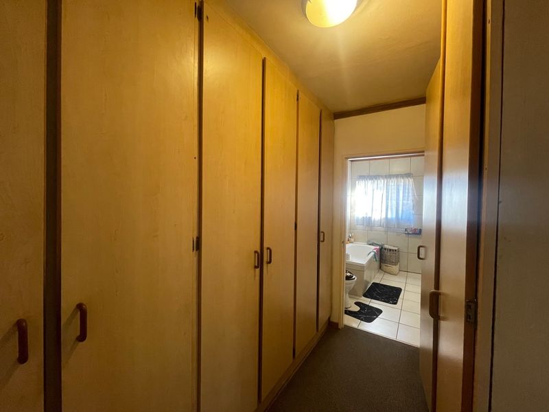 A hallway featuring extensive built-in wooden cupboards, providing ample storage space and leading directly into a bathroom.