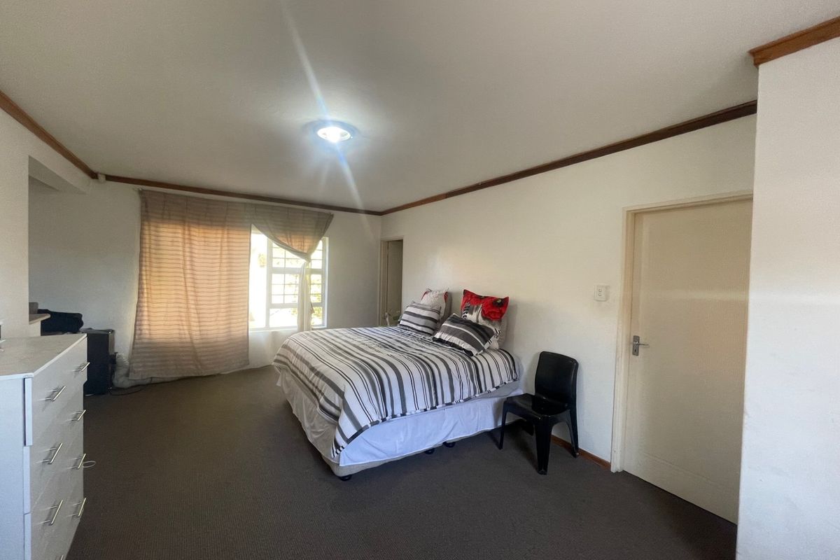 A spacious bedroom featuring neutral walls, carpeted flooring, and timber ceiling trim, offering a functional and well-lit living space.