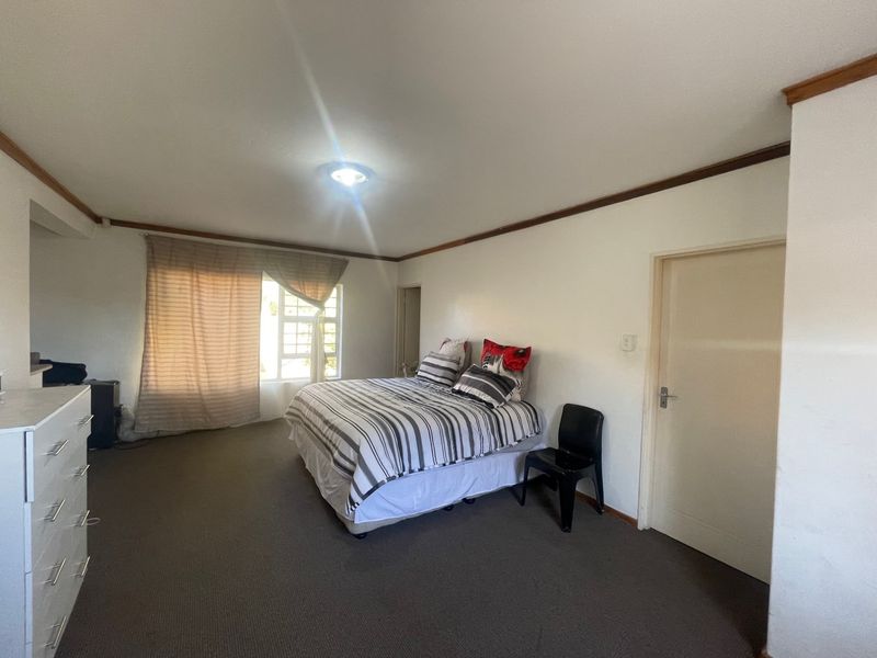 A spacious bedroom featuring neutral walls, carpeted flooring, and timber ceiling trim, offering a functional and well-lit living space.