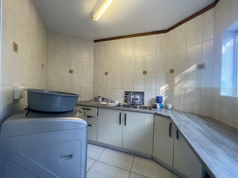 A functional laundry room featuring built-in cabinetry, a laminate countertop, a stainless steel sink, and full-height wall tiling.