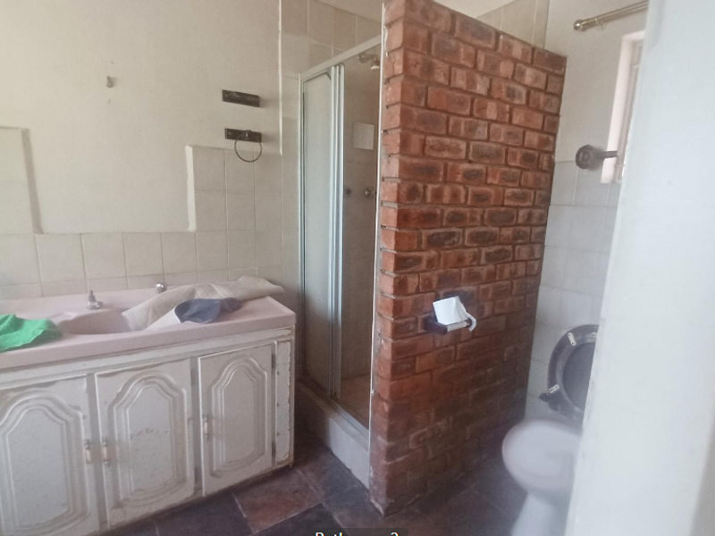 A dated bathroom featuring a vanity unit, a shower enclosure with an exposed brick partition, and a standard toilet.