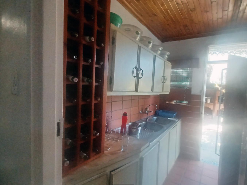 A functional scullery area featuring built-in wine storage, upper and lower cabinetry, a stainless steel sink, and a timber-clad ceiling.