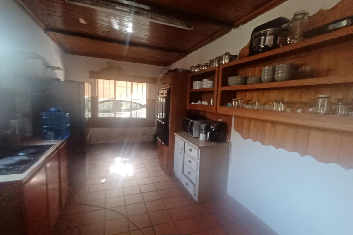 A dated kitchen featuring wooden cabinetry, open shelving, a built-in oven, and tiled flooring with a wooden ceiling.