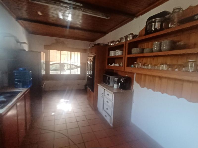 A dated kitchen featuring wooden cabinetry, open shelving, a built-in oven, and tiled flooring with a wooden ceiling.