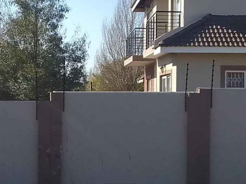 Exterior view of a townhouse featuring a perimeter wall with electric fencing and a balcony with metal balustrades.