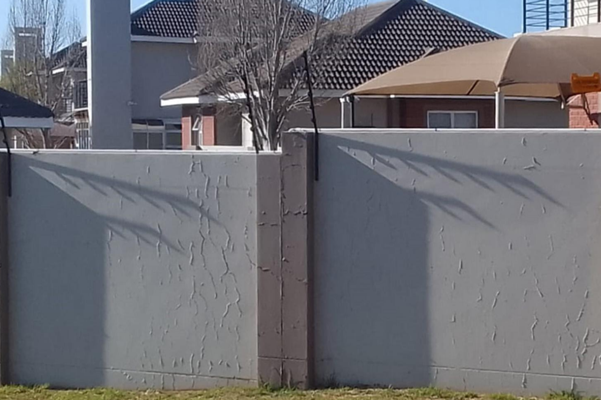 A view of the property's rear boundary wall featuring precast concrete panels and installed electric fencing, showing signs of weathered paint.