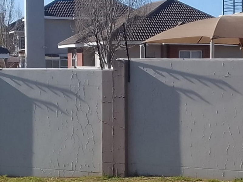 A view of the property's rear boundary wall featuring precast concrete panels and installed electric fencing, showing signs of weathered paint.
