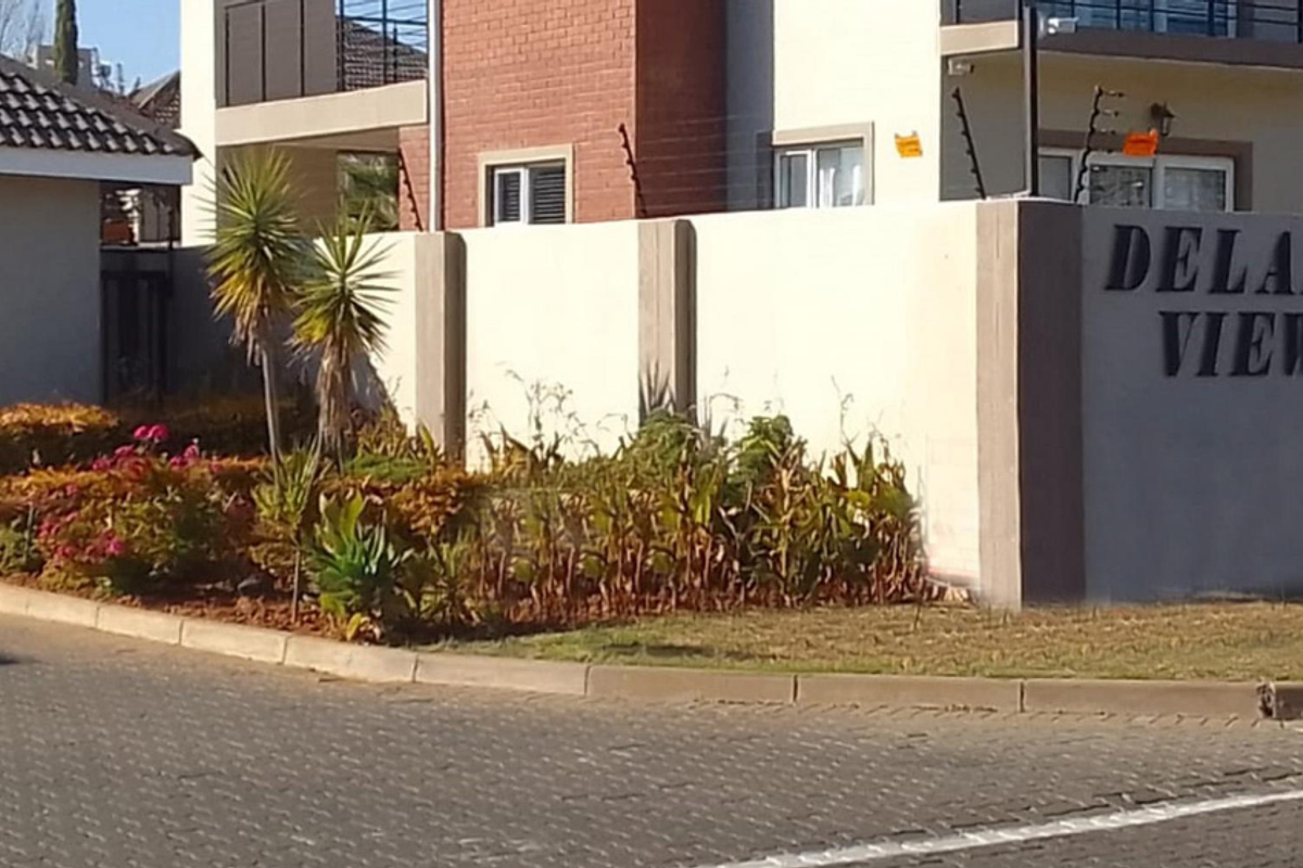 Front entrance view of Delano View townhouse complex featuring a secure boundary wall, electric fencing, and established garden landscaping.